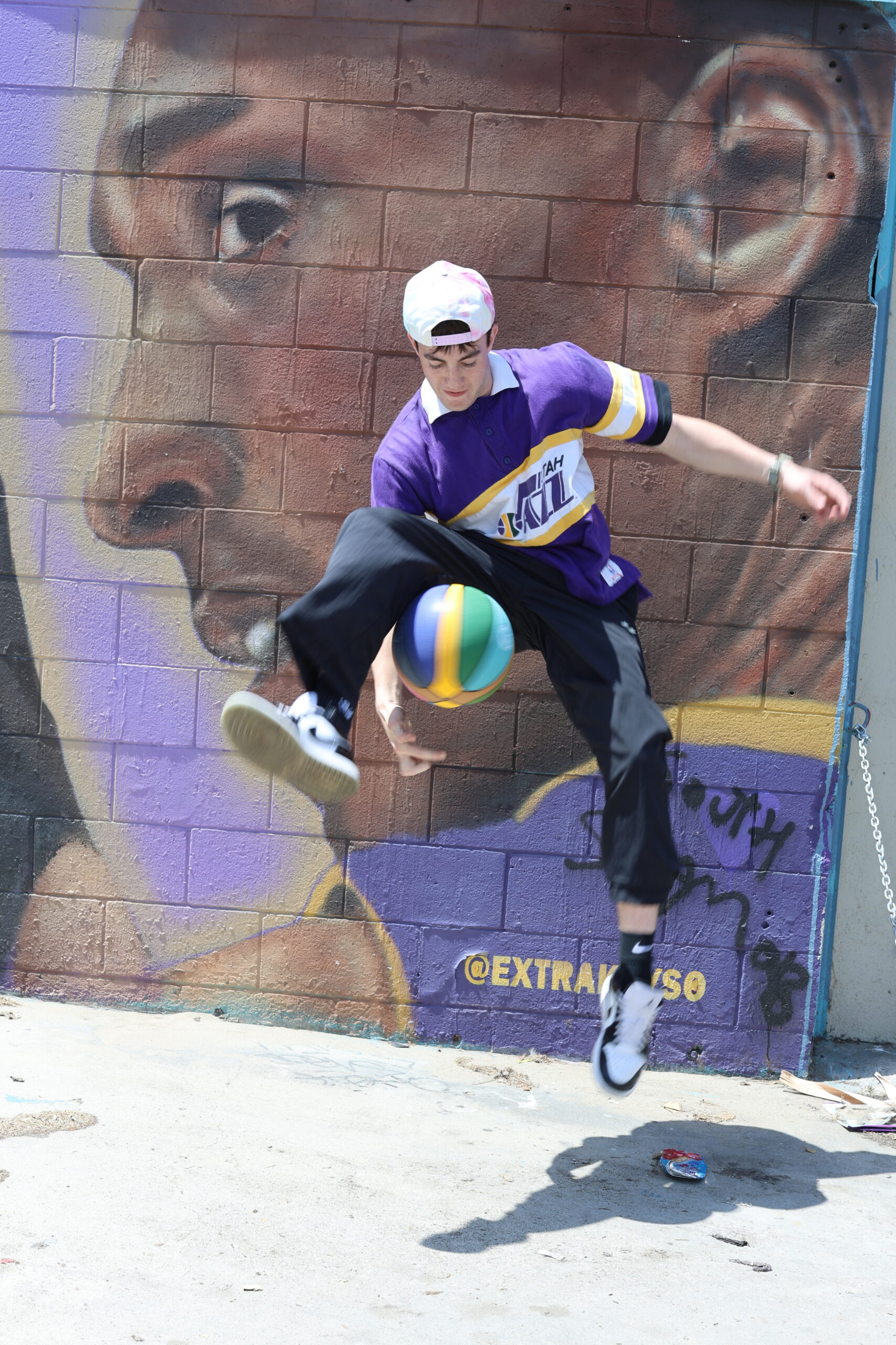 McDeezy spinning a basketball mid-jump in front of a Kobe Bryant mural